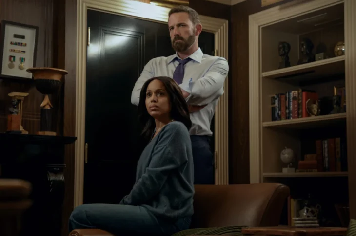 "A woman sits on a leather chair looking concerned, while a man stands behind her with arms crossed in a dimly lit office or library filled with shelves, books, and decorative objects."